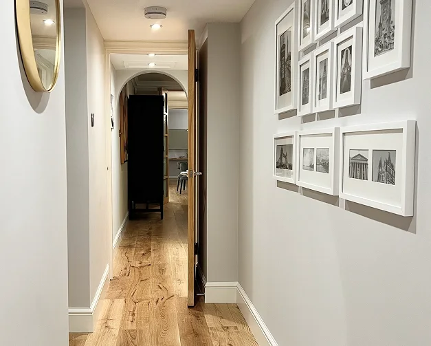 Renovated Kensington apartment hallway with framed artwork and oak flooring.