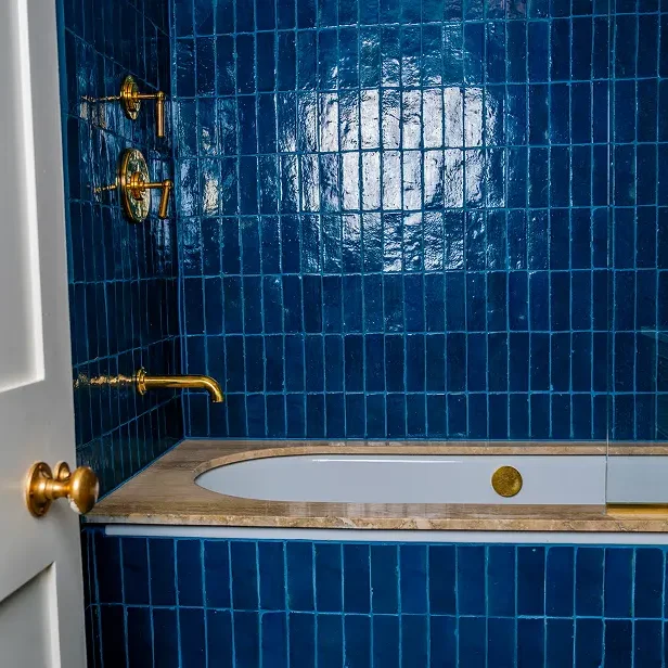 Bathroom renovation London with bathtub, brass fixtures, and blue wall tiles.