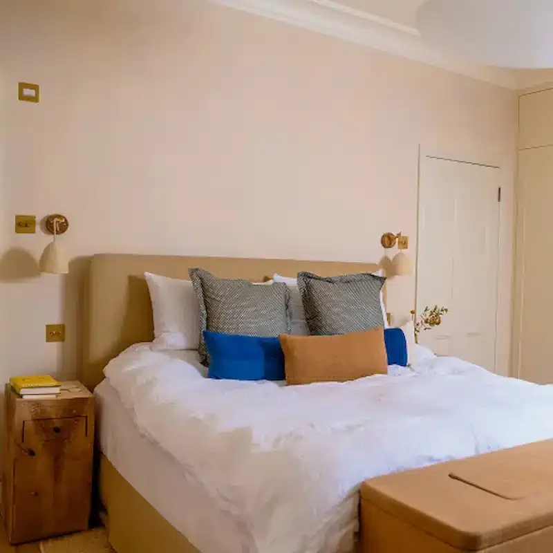 Renovated bedroom in a Notting Hill home with upholstered headboard, fitted storage and warm neutral finishes.