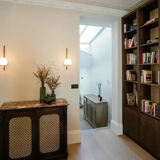 Renovated living room leading into a bright rear space with bespoke shelving and wall lights.