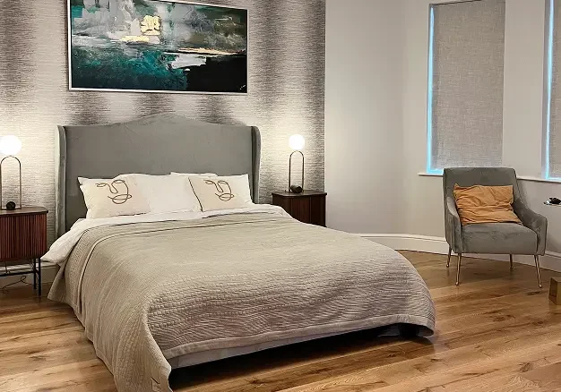 Contemporary bedroom in Kensington apartment renovation with grey headboard and modern art.