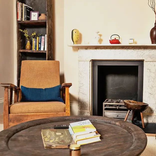 Victorian house renovation in Notting Hill featuring rustic coffee table, armchair, and marble fireplace.