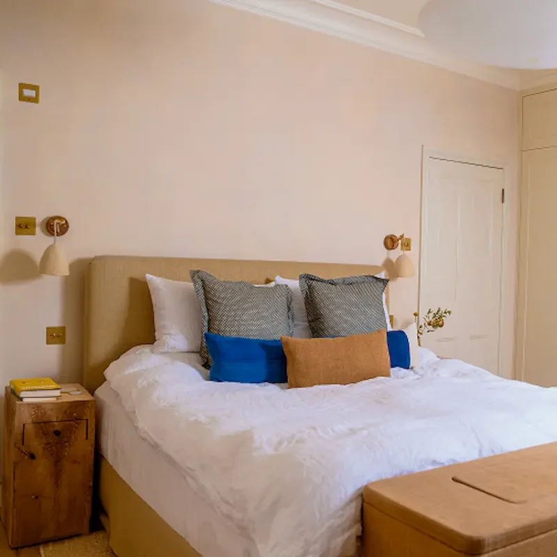 Refurbishment company bedroom with upholstered headboard, layered cushions, and natural colour palette.